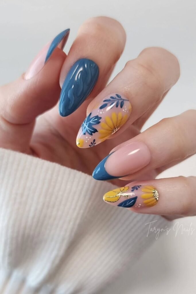 A soft nude base paired with bold blue and yellow accents creates a fresh and artistic nail design. Vibrant sunflower nail art on select nails brings a playful yet elegant touch, blending geometric and floral elements for a unique look.